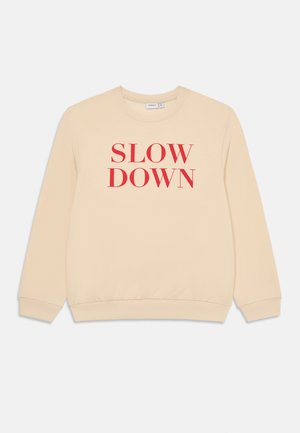 Beige hettegenser med rød "SLOW DOWN" tekst. Har rund hals, ribbestrikkede mansjetter og en avslappet passform. Laget av bomull, myk tekstur.
