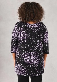 Černá tunika s fialovým květinovým vzorem, má tříčtvrteční rukávy a kulatý výstřih, měkká látka s mírně volným střihem.