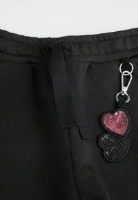 Czarne dresowe spodnie z materiałowym sznurkiem, z akcentem w postaci breloka w kształcie dwóch świecących serc w kolorze różowym i czarnym.