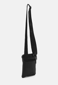 Černá kožená kabelka přes rameno s texturovaným povrchem, obsahující přihrádku na zip a nastavitelný popruh s páskou s logem.