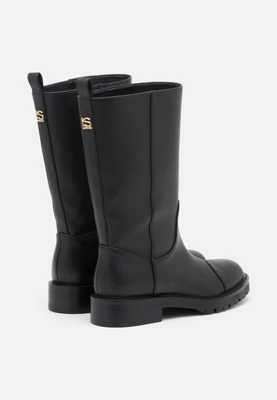Botines de cuero negro con una textura suave, puntera redondeada y un tacón ligeramente grueso. Acentos de hardware dorado notables en los laterales.