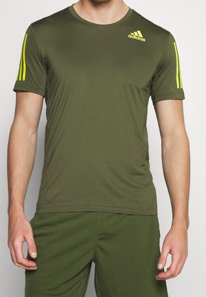 Homme portant un t-shirt de sport Adidas vert olive avec des bandes jaunes sur les manches et le logo Adidas sur la poitrine, associé à un short assorti.