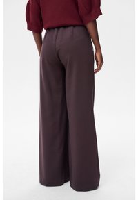 Spodnie o szerokich nogawkach w ciemnofioletowym materiale, charakteryzujące się gładką fakturą i elastycznym pasem dla wygody. Minimalistyczny design bez widocznych detali.