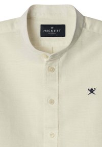 Camisa de lino color crema con cuello vuelto, cinco botones y un pequeño logo bordado en navy en el lado izquierdo del pecho.
