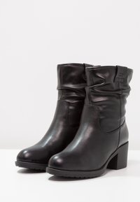 Bottes noires en cuir à la cheville avec un design froncé, bout arrondi et talon bloc. Texture lisse avec des coutures minimales et un accent simple.