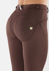 Leggings marroni con una texture liscia, dotati di una tasca posteriore e un accento distintivo del logo vicino alla vita. Design slim-fit.