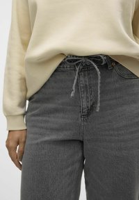 Pulover bej cu manșete ribbate, asortat cu blugi gri din denim. Blugii au un talie cu șnur și un model texturat subtil.