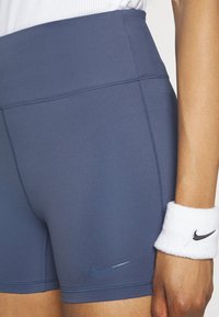Gros plan d'une personne portant un short de sport Nike bleu et un bandeau de poignet Nike blanc sur son bras droit.