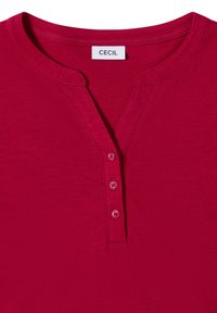 Rød kortærmet top med v-halsdesign, der har en stolpe med tre knapper og et glat, struktureret stof. Etiketten læser "CECIL."