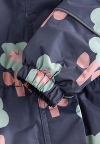 Jachetă impermeabilă bleumarin cu manșete elastice, având un model cu flori verzi zâmbitoare și accente roz. Textură netedă, material durabil.