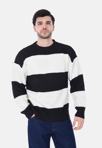 Maglione a strisce bianche e nere con un motivo testurizzato, scollatura rotonda e polsini a costine, abbinato a jeans in denim blu.