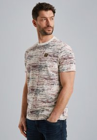 Hvid T-shirt med korte ærmer og et multicolor abstrakt mønster i rødt og sort. Har en rund halsudskæring og et lille mærke på brystet.