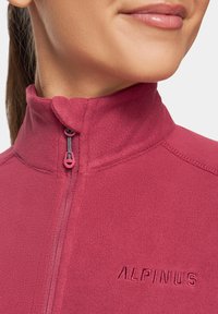 Kurtka polarowa w kolorze burgundowym, z wysokim kołnierzem, zamkiem błyskawicznym z uchwytem oraz haftowanym logo "ALPINUS" na piersi. Miękka tekstura.