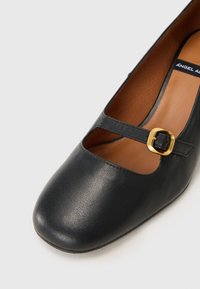 Black leather shoe with rounded toe and cut-out detail, featuring a narrow strap and rectangular gold buckle. Smooth texture and low heel.