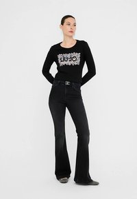 Črno dolgo majico z dolgimi rokavi, okrašeno z cvetličnim vzorcem in napisom "LIU JO", kombinirano s temnimi zvončastimi kavbojkami s sijočim zaponko na pasu.