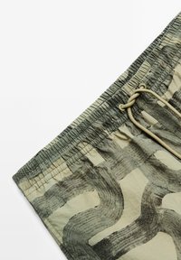 Leichte, beige Shorts mit abstrakten, dunkelgrauen Mustern, ausgestattet mit einem elastischen Bund und Kordelzug für eine verstellbare Passform.