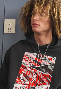 Sort hoodie med multikolor grafisk print, der indeholder rød, hvid og grå tekst. Teksten lyder "DU KAN GØRE ALT." Sølv kædedetalje.