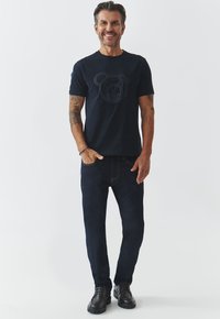 Jūros laivyno T-shirt su toniniu lokio grafiku, derinama su tamsiai mėlynomis džinsomis ir juodais tvirtais batais. Paprastas dizainas, standartinė prigludimo forma, medvilnės audinys.