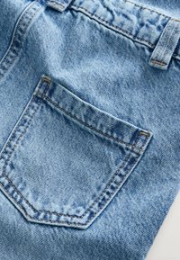 Lichtblauwe denim stof met een achterzak met zichtbare stiksels. De textuur is soepel met hier en daar een lichte kreuk.