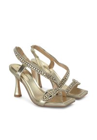 Sandalias de tacón alto doradas con tiras anchas adornadas con rhinestones, que presentan una punta cuadrada y un diseño de tacón delgado.