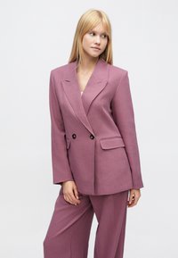 Lila zweiteiliger Anzug mit einem maßgeschneiderten, zweireihigen Blazer mit Reverskragen und weitem Bein, gefertigt aus einem strukturierten Stoff.