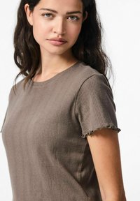 Kahvin lyhythihainen t-paita, joka on valmistettu karkeasta kankaasta, jossa on uritettu kuvio ja rispaantuneet reunat hihoissa; pyöreä kaula-aukko ja rento malli.