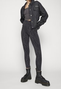 Person i svart kort denimjacka från Adidas, grå randig crop top, svarta och grå zebra-mönstrade leggings och svarta snörda platåstövlar.