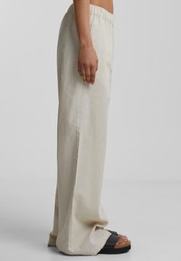 Ljust beige vida byxor med elastiskt midjeband, tillverkade av mjukt tyg. Har en jämn textur och faller mjukt till golvet.