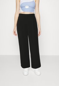 Schwarze weite Hosen aus weichem Stoff, mit vorderen Falten und einem glatten Taillenbund, kombiniert mit einem hellblauen Crop-Top und weißen Turnschuhen.