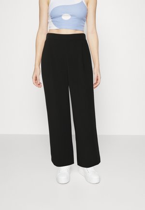 Zwarte wijde broek van zachte stof, met voorplooien en een gladde tailleband, gecombineerd met een lichtblauwe crop top en witte sneakers.