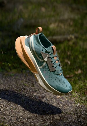 Light blue athletic shoe with perforated upper, orange accents, and a cushioned sole. Features a textured surface and lace-up design.