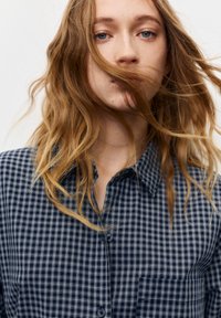 Navy and white checkered button-up shirt featuring a collar, button closure, and a chest pocket, with soft fabric and a relaxed fit.