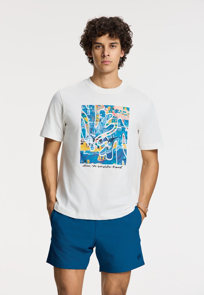 Camiseta de algodón blanca con un diseño gráfico azul que representa una vibrante escena costera, combinada con pantalones cortos azul sólido. Mangas cortas, cuello redondo.