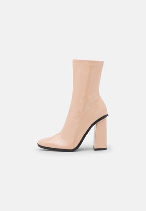 Bottine en cuir verni nude brillant avec bout carré et talon épais haut en bloc, semelle noire et surpiqûres décoratives.