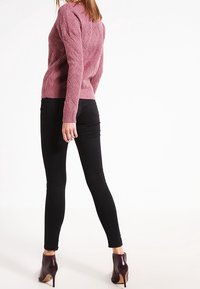 Maglione rosa lavorato a maglia con un motivo a diamante testurizzato, abbinato a jeans skinny neri e scarpe con tacco bordeaux.