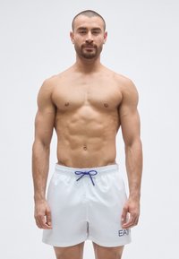 Fehér fürdőnadrág kék húzózsinórral, bal lábszáron hímzett logóval. Az anyag sima és könnyű megjelenésű.