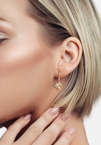 Guldtonede drop øreringe med et diamantformet design, der har udskårne mønstre og en lille klar accentsten.