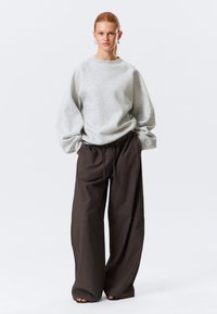 Sudadera gris con mangas oversized combinada con pantalones holgados de color marrón oscuro. La tela parece suave, con un corte relajado y cintura elástica.