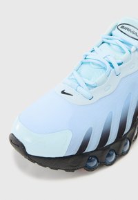 Vaaleansininen Nike Air Max -lenkkari, jossa on teksturoitu verkkopinta, mustia yksityiskohtia ja erottuva kuplamainen pohja, jossa on sinisiä vaimennuselementtejä.