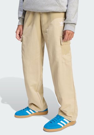 Beige Cargo-Hosen mit Seitentaschen, kombiniert mit blauen Turnschuhen mit weißen Streifen. Strukturierter Stoff und lässige Passform.