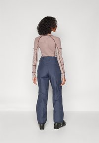 Μακρυμάνικο, μπορντό πουκάμισο με σχέδιο και στενή γραμμή, συνδυασμένο με χαλαρούς μπλε παντελόνες, φτιαγμένες από ανθεκτικό ύφασμα με τσέπες με φερμουάρ.