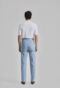 Pantalones azul claro con un ajuste entallado, que presentan bolsillos traseros con botones dorados, combinados con una camisa blanca de manga corta ajustada.