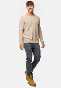 Vaaleanbeige pitkähihaisesta neulepaidasta, harmaista slim fit -farkuista ja vaaleista nauhakenkistä, joissa on teksturoitu pohja, taustana pelkkä valkoinen tausta.