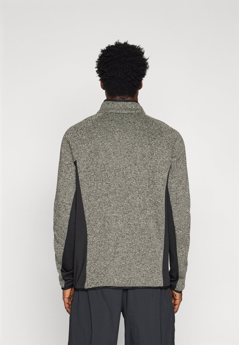 Szara polarowa kurtka z wysokim kołnierzem, czarnymi bocznymi panelami i teksturowanym korpusem. Długie rękawy i luźny krój, idealny do noszenia warstwowo.