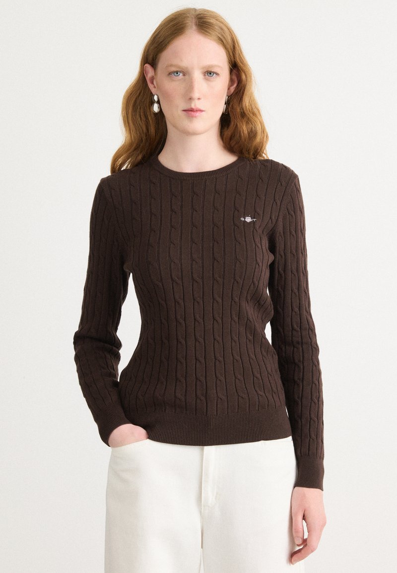 Pull en tricot marron avec une texture côtelée, doté d'un col rond classique et de manches longues. Petit logo sur la poitrine.