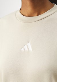 Bežna bombažna pulover s strukturo, ki ima rebrasto ovratnico in belo izvezeno Adidasovo logotip na levem prsnem delu. Gladka tekstura, sproščen dizajn.