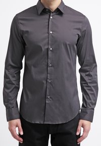Mörkgrå långärmad skjorta med knappar i ett mjukt tyg. Har en klassisk krage och sju framknappar. Skräddarsydd passform med rundad fåll.