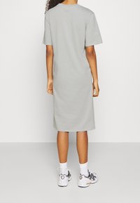 Valkoinen harmaa t-paitamekko, polvipituinen, lyhyet hihat, pyöreä kaula-aukko, puuvillakangasta, yhdistettynä valkoisiin ja mustiin lenkkareihin ja valkoisiin sukkiin.