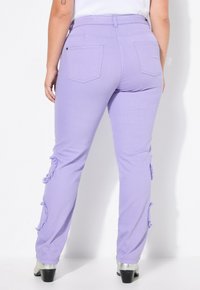 Pantalones de mezclilla lila con detalles deshilachados en los laterales, diseño de cinco bolsillos y cintura alta. Completados con botas de tacón plateadas.