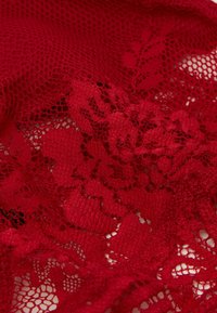 Red lace fabric featuring a floral pattern and open weave, with a soft texture. The design includes intricate detailing and layered sections.